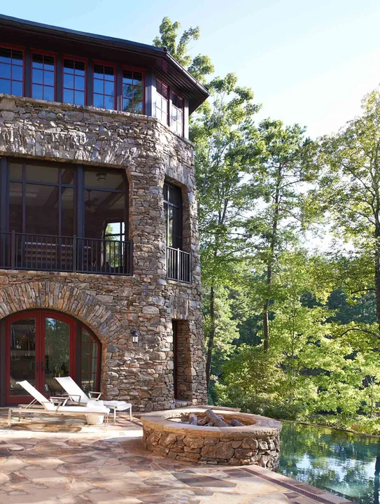 Tall stone home with fire pit and infinity pool.